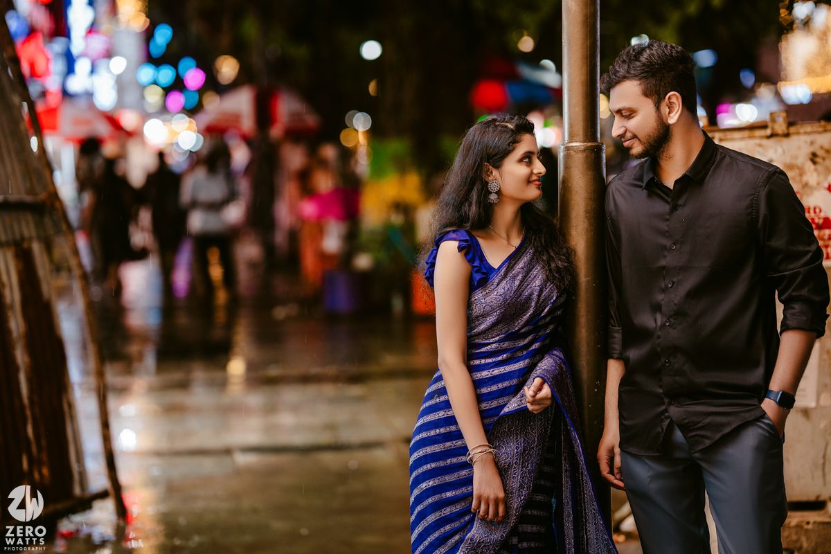 A romantic nighttime street scene with colorful lights and a couple in traditional Indian attire.