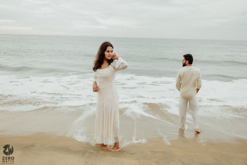 A dreamy beach scene with couple in white outfits playing by the ocean waves.