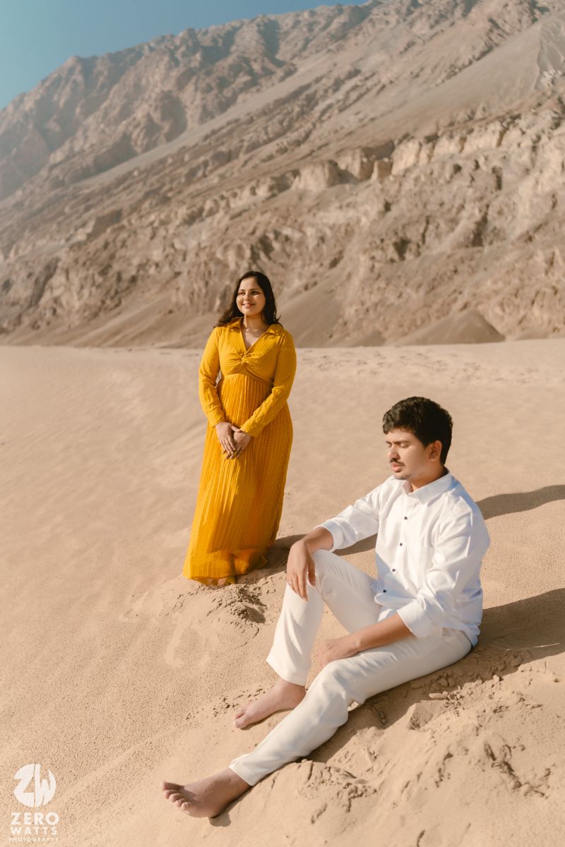 Couple in casual wear posing for a desert photoshoot against rocky mountain backdrop.
