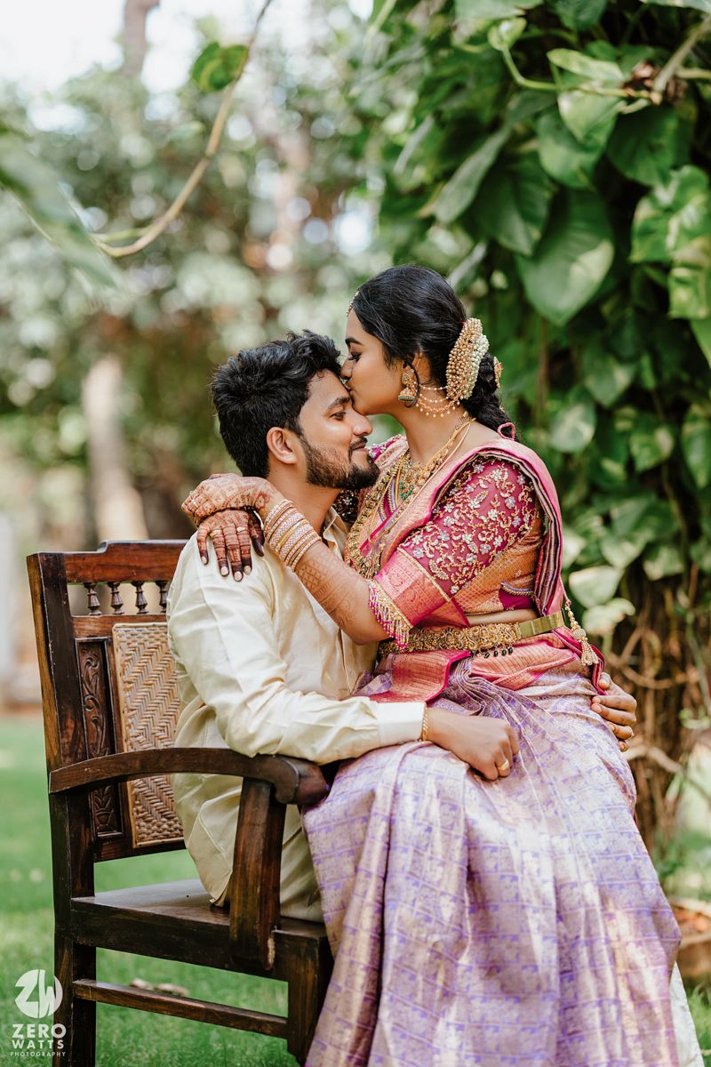 Intimate moment of couple in traditional South Indian wedding attire on wooden chair.