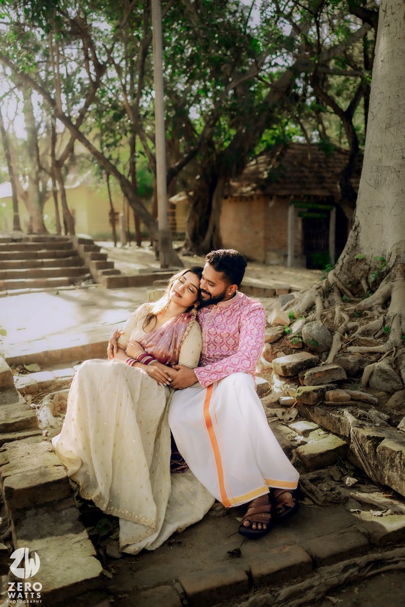 Couple in traditional Indian attire relaxes on ancient stone steps surrounded by trees.