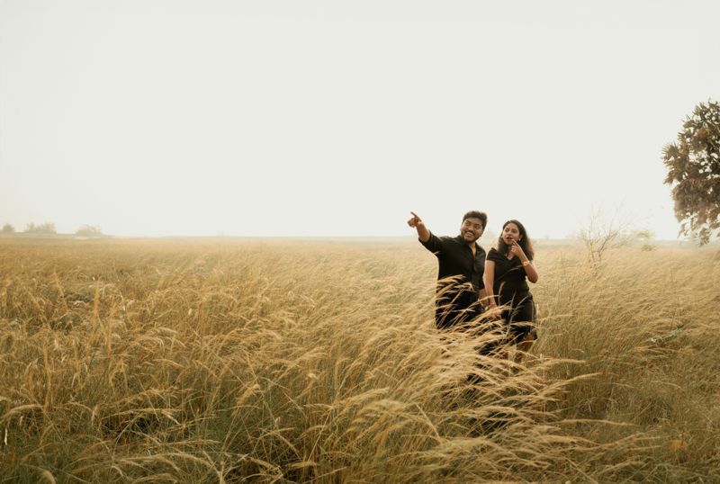 Two people stand together in a tall grass field gesturing upward during golden hour.