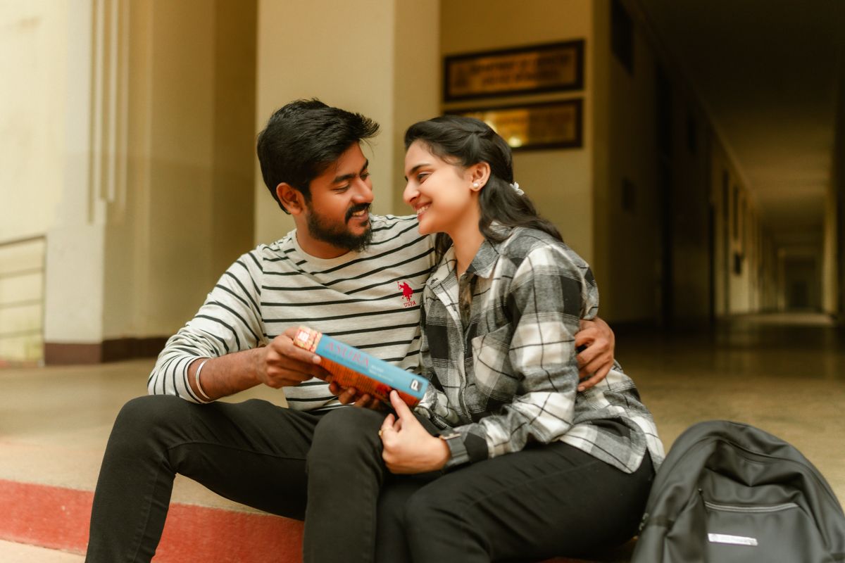 A couple sits close together on steps in a college hallway, sharing a warm moment.