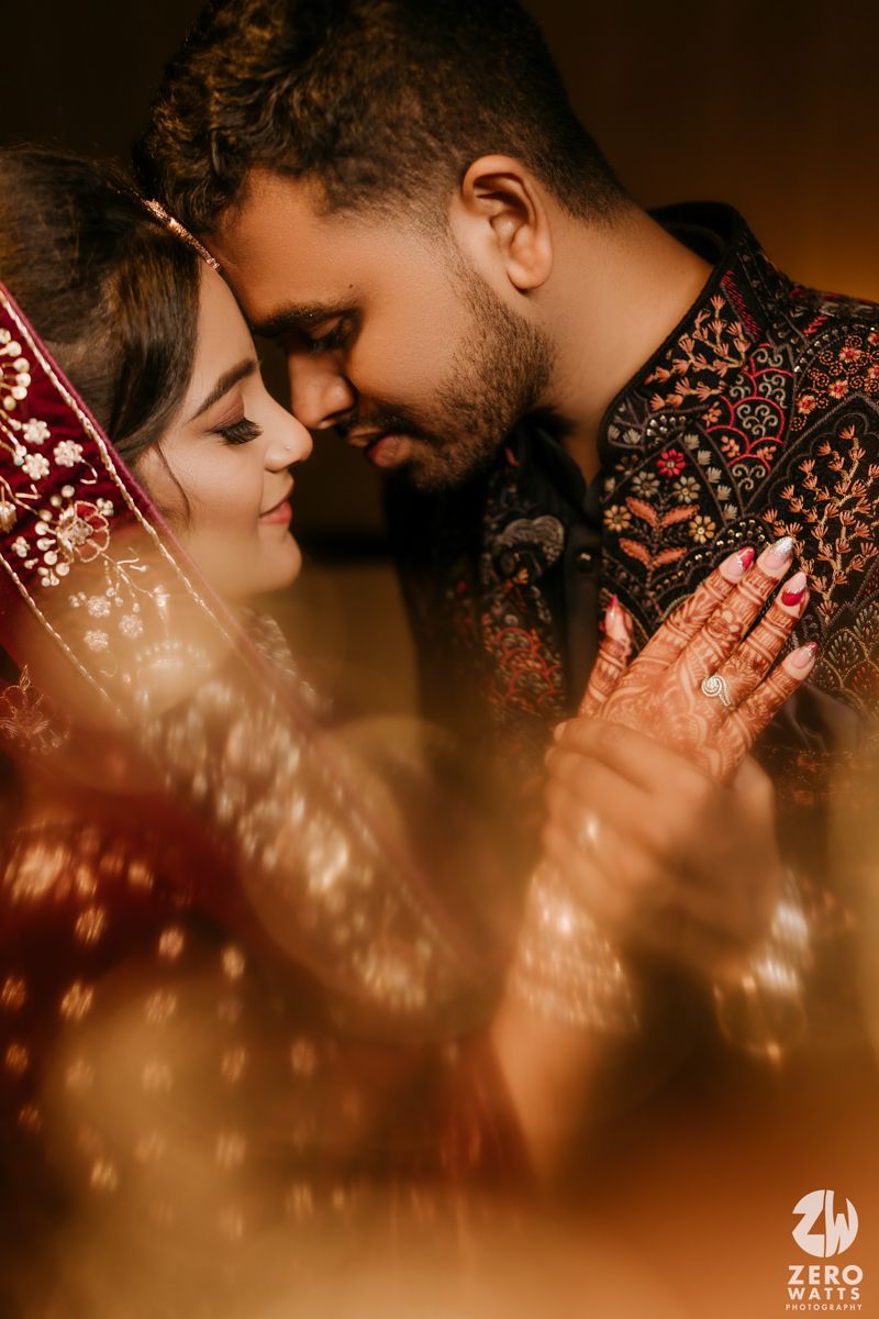 Intimate wedding portrait with intricate henna designs and traditional outfits captured in romantic golden light.