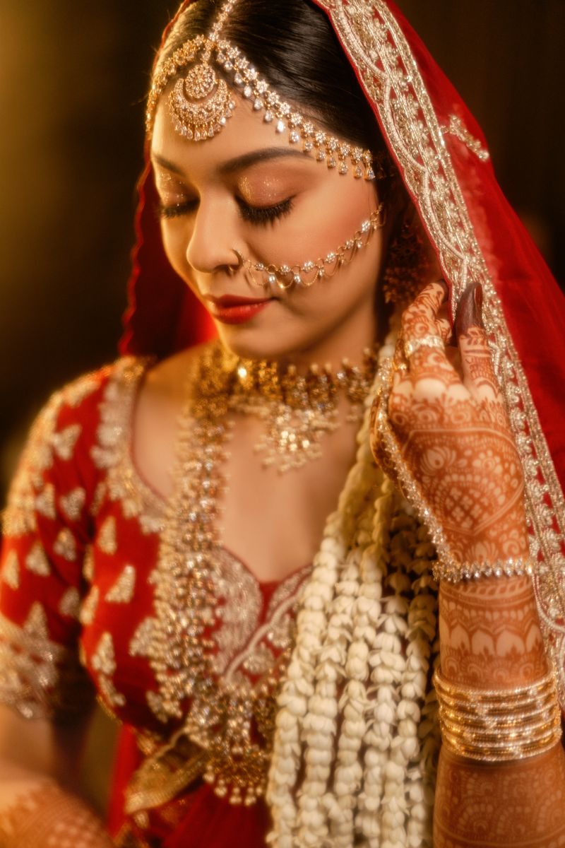 Traditional South Asian bridal attire with intricate gold jewelry, mehndi designs and a red embroidered veil.