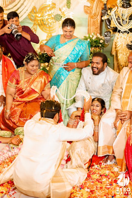 Joyous moment at an Indian wedding ceremony as guests gather amidst bright flowers and traditional decorations.