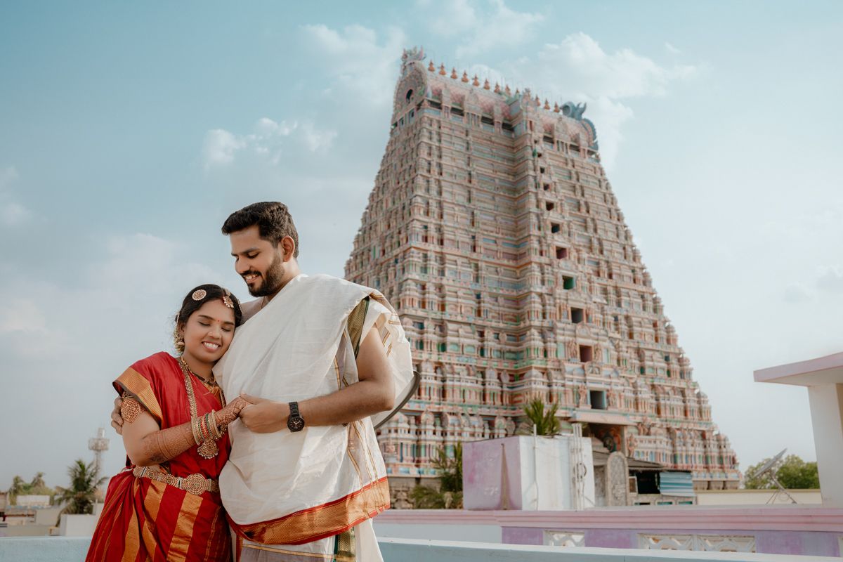 A South Indian temple with a towering gopuram decorated with ornate architecture stands against a bright blue sky.