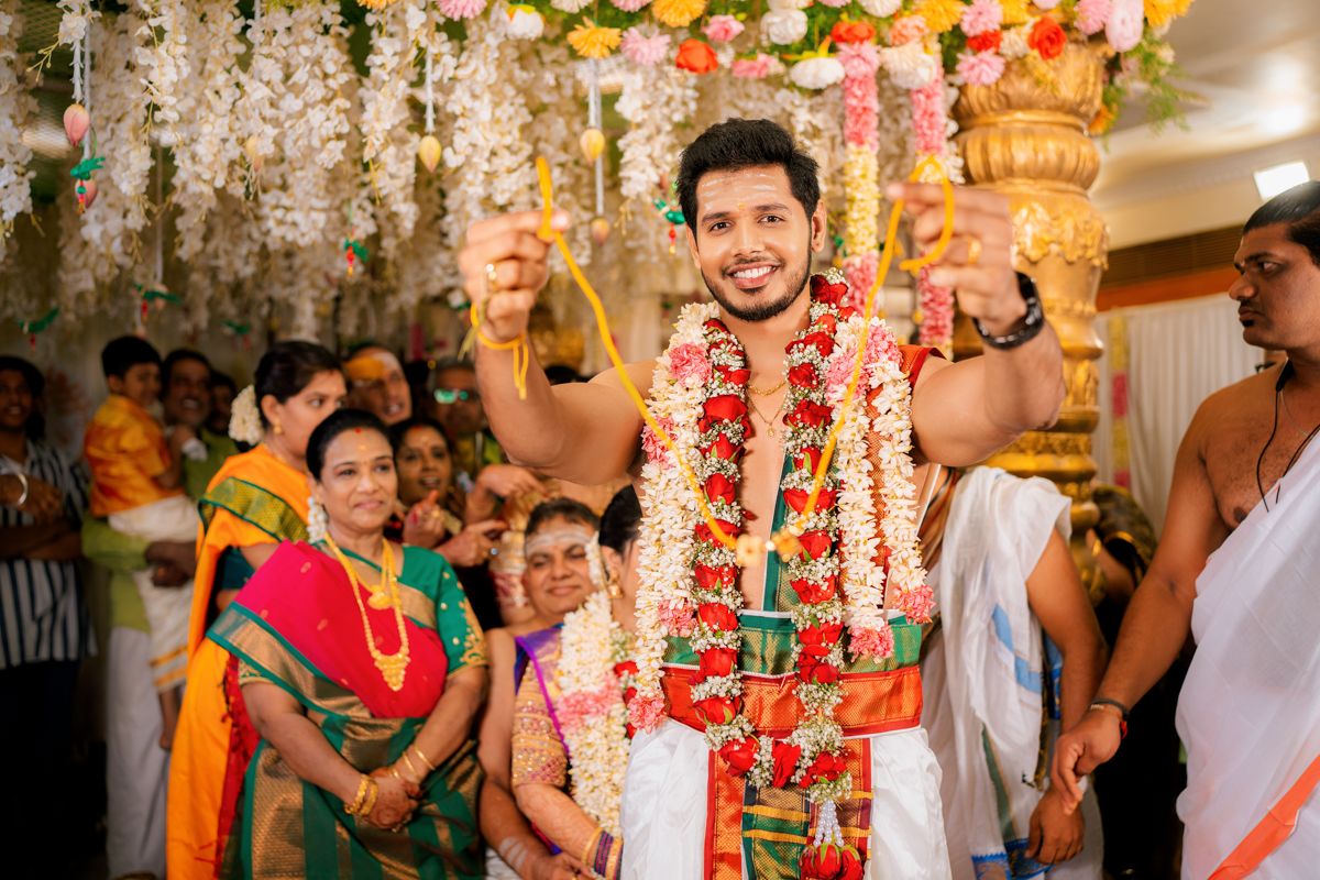 Celebratory moment during traditional Indian wedding ceremony with decorative floral arrangements and chandeliers overhead.