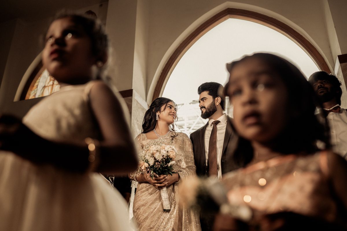 Wedding couple standing between blurred figures in an elegant arched doorway with romantic lighting.