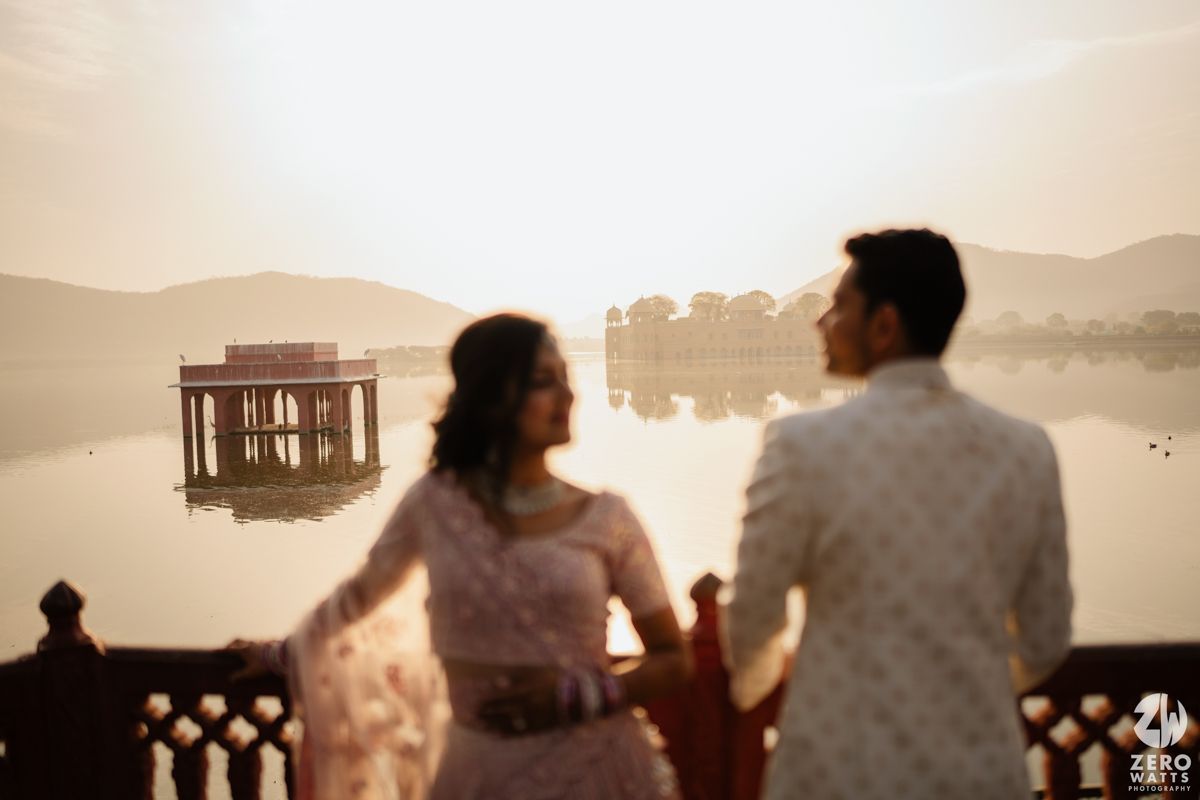 Two silhouettes hold hands on a deck at dusk with a tranquil lake and mountains creating a dreamy atmosphere.