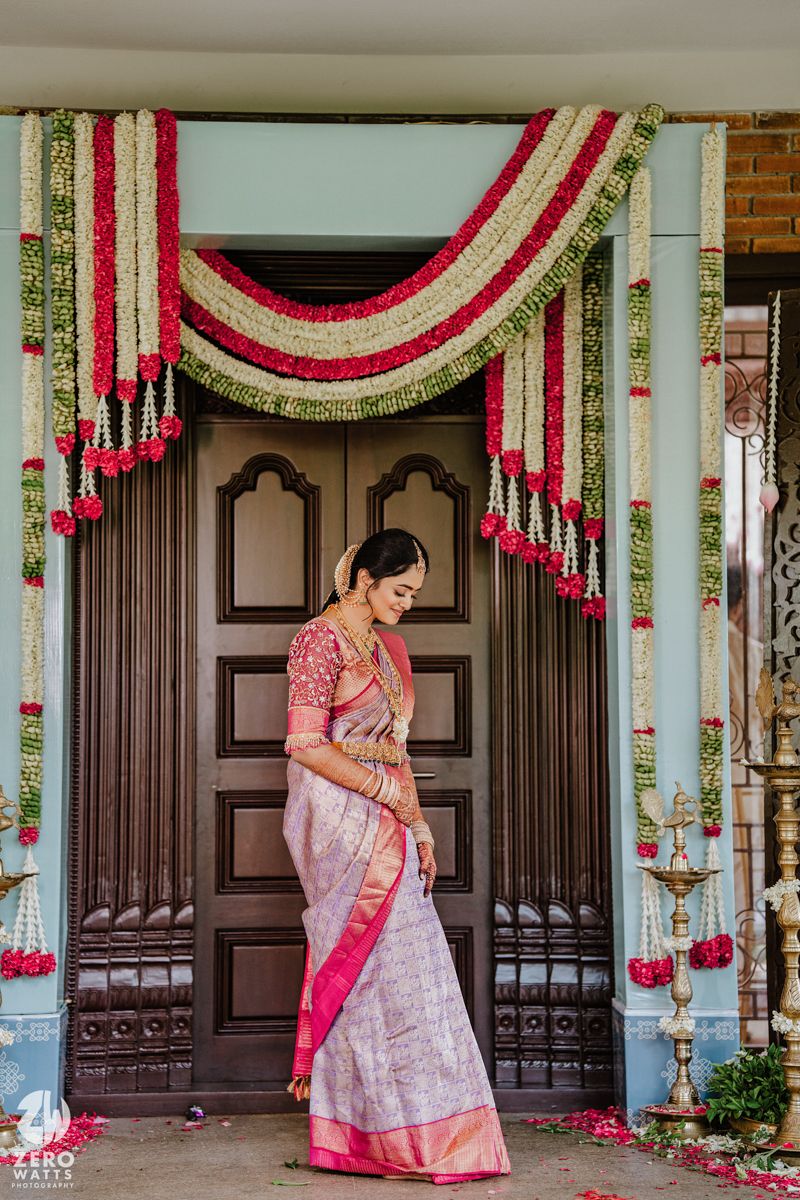 Traditional South Indian bride in pink and white saree under floral wedding decor.
