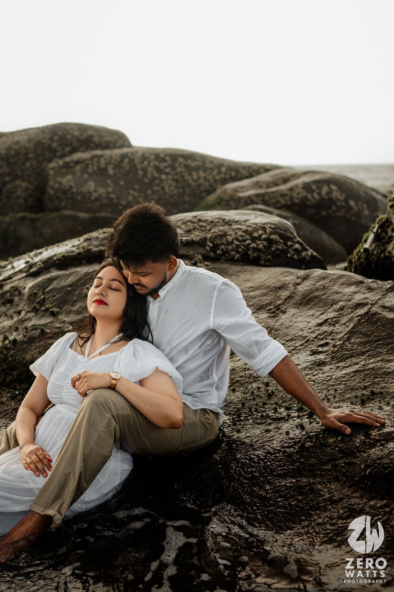 A romantic couple embraces on rocky coastal cliffs during a moody photoshoot at sunset.