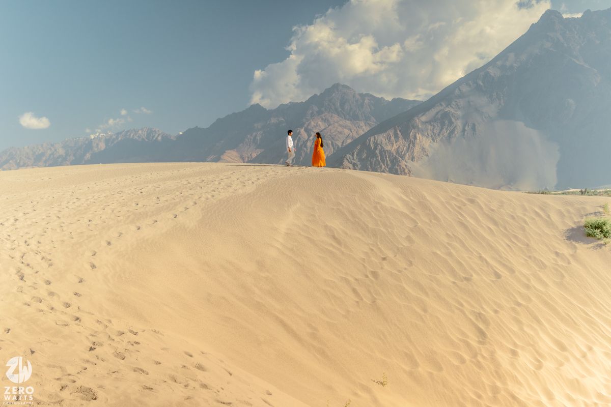 Desert sand dunes and mountains create a dramatic landscape under cloudy skies.