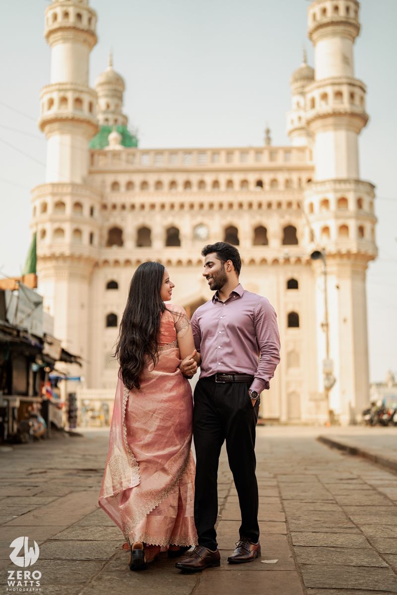 A couple poses romantically in front of the historic Charminar monument in Hyderabad wearing traditional Indian attire.