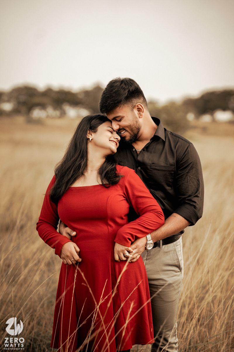 A gentle embrace between a couple in a wheat field wearing complementary red and black attire.