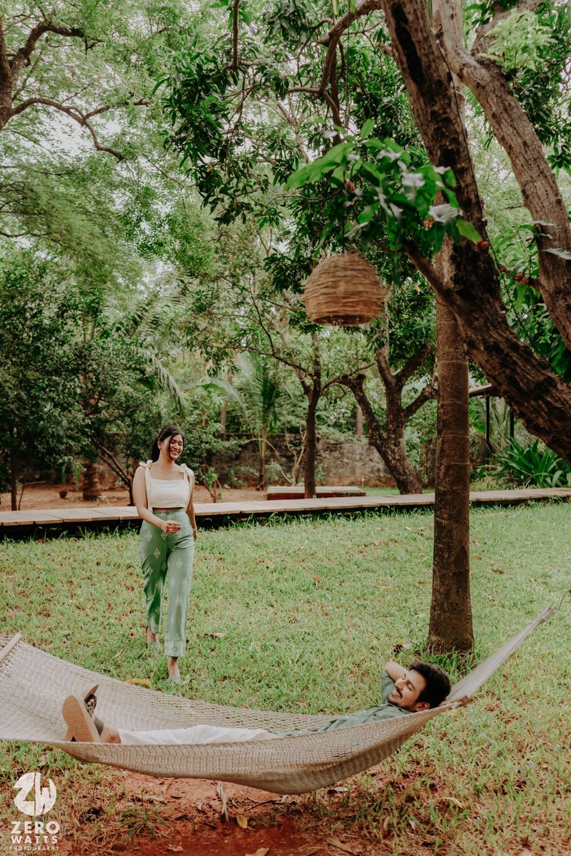 A hammock hangs between two trees in a lush green garden setting with dappled sunlight filtering through the leaves.