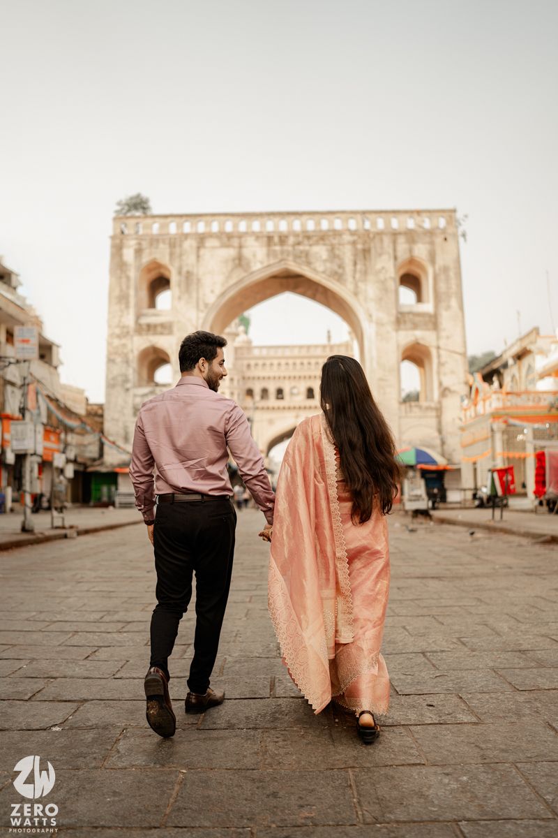 A couple walking hand in hand towards a historic Indian archway in traditional clothing.