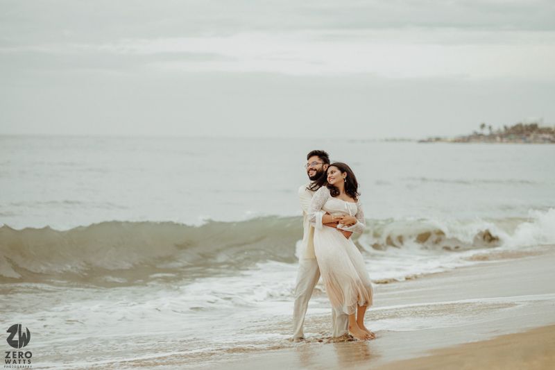 Couple walking along a misty beach shore during golden hour.