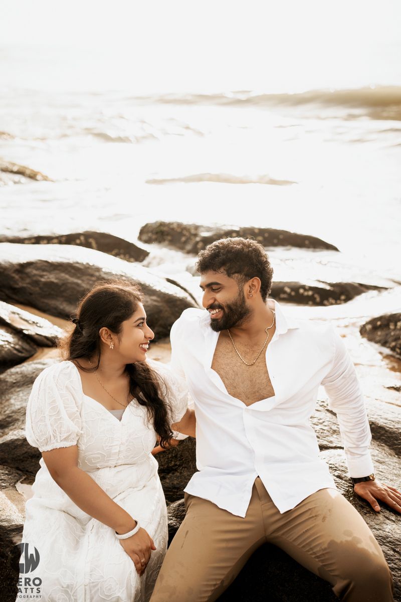 Happy couple sharing joyful moment while sitting on beach rocks.