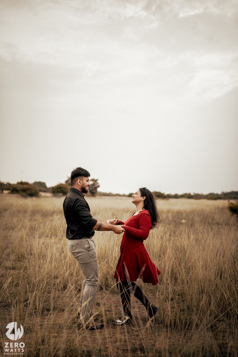 A couple dances together in a golden field during sunset wearing a red dress and casual attire.