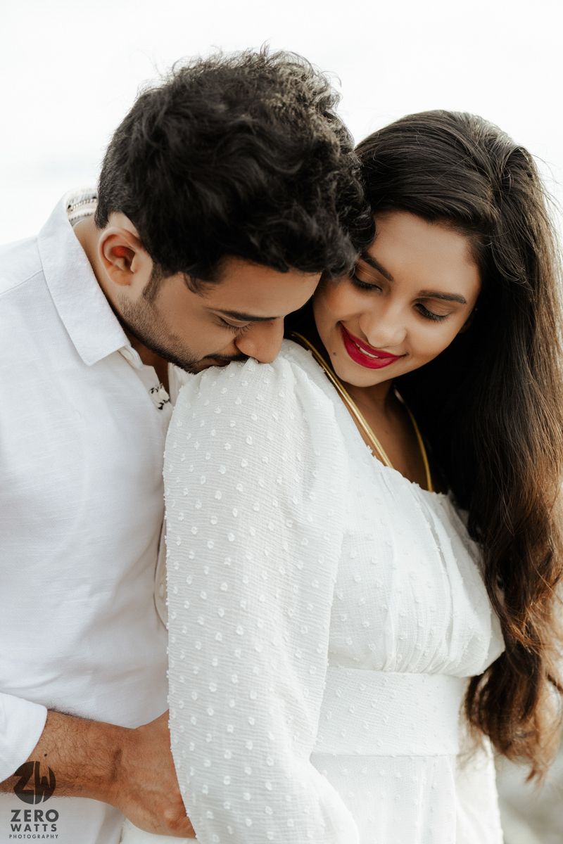 An intimate romantic moment captured between a couple wearing white outfits against a light background.