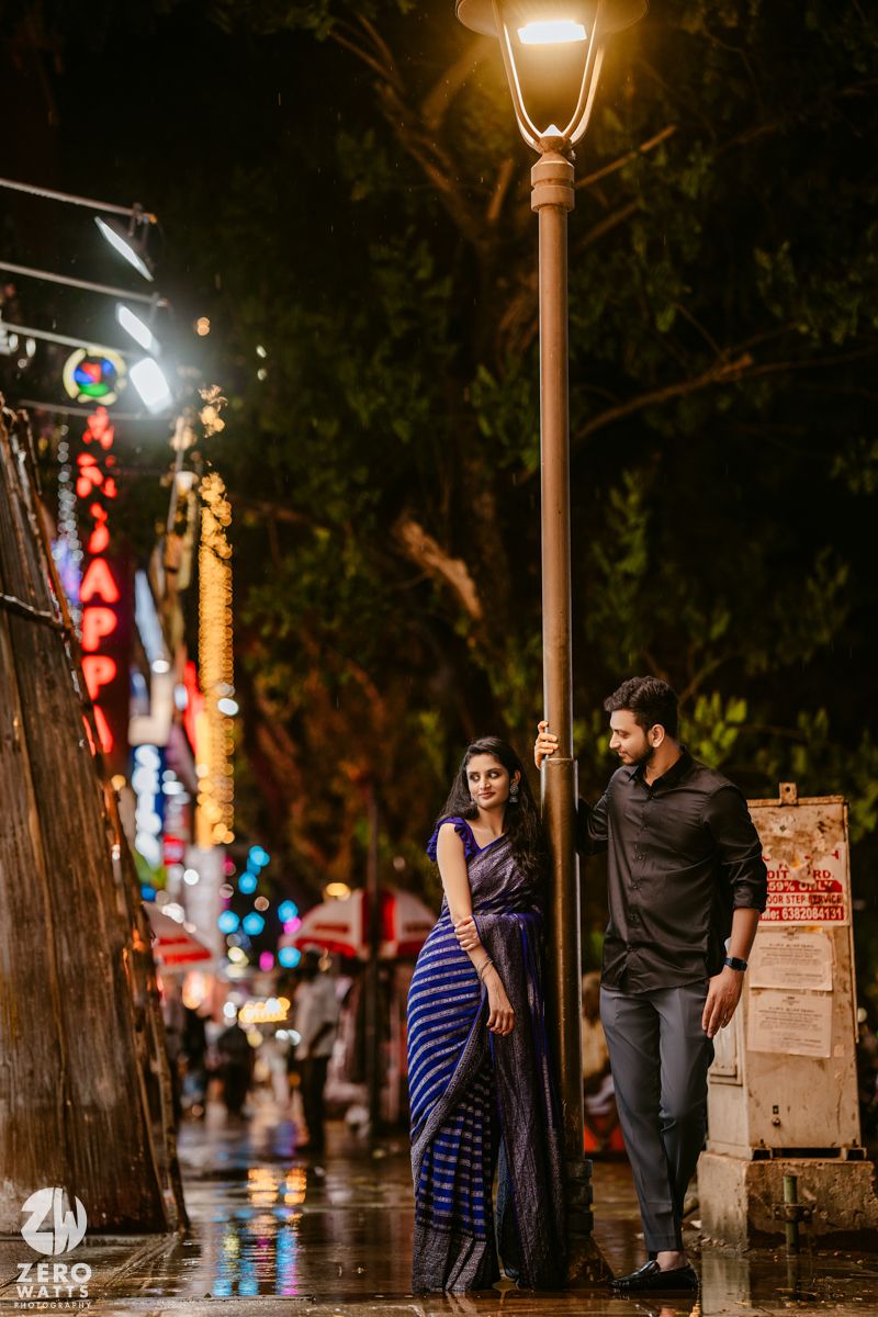 A nighttime street scene with a couple standing under a lamppost amid colorful city lights.