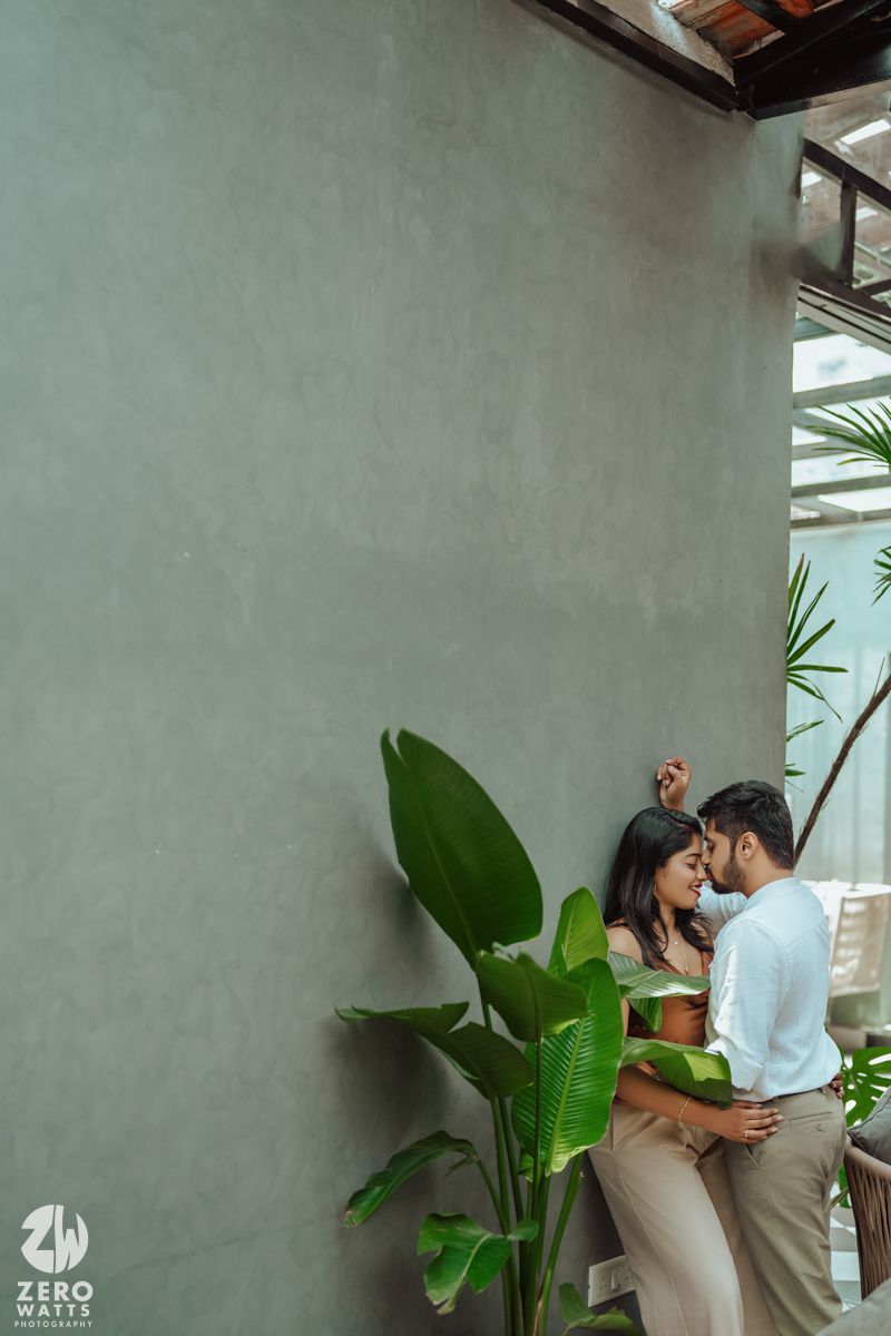 An intimate moment between couple near tropical plants against minimalist grey wall.