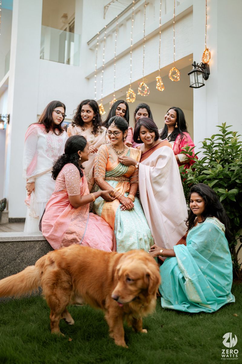 A festive gathering outdoors with people in pastel ethnic wear and a golden retriever joining the celebration.