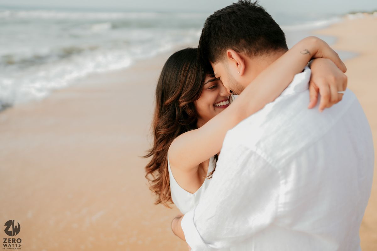 Intimate embrace between couple in white clothing on sandy beach.