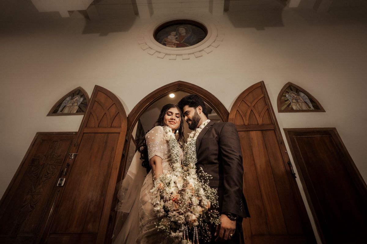 A romantic wedding portrait framed by wooden church doors and arched architecture.
