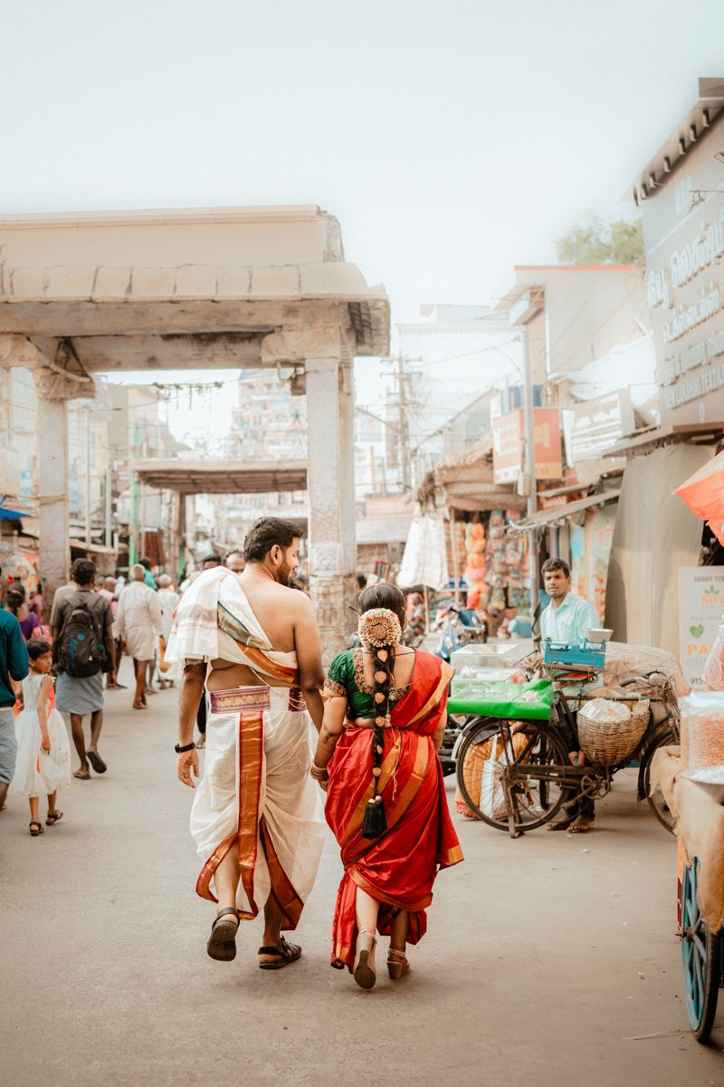 A couple in traditional Indian attire walks through a busy street market with vendors and shops in Chennai, India.