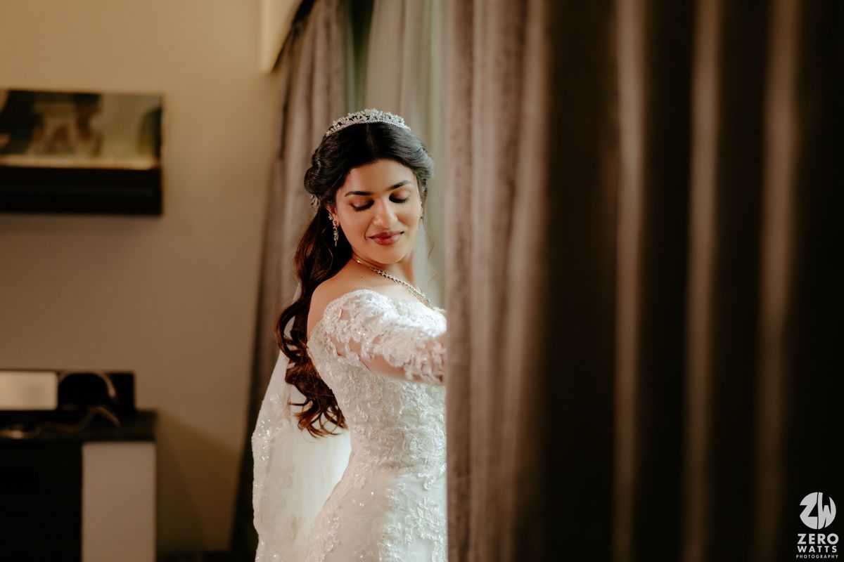 Close-up portrait shot of bride wearing delicate long-sleeved lace wedding dress in warm indoor lighting.