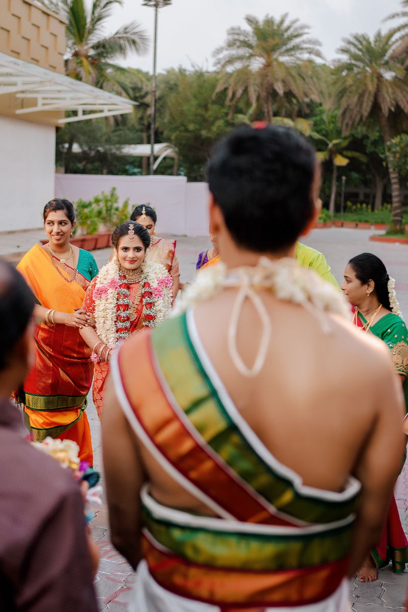 Wedding guests in colorful traditional Indian attire gather outdoors near palm trees during a ceremony.