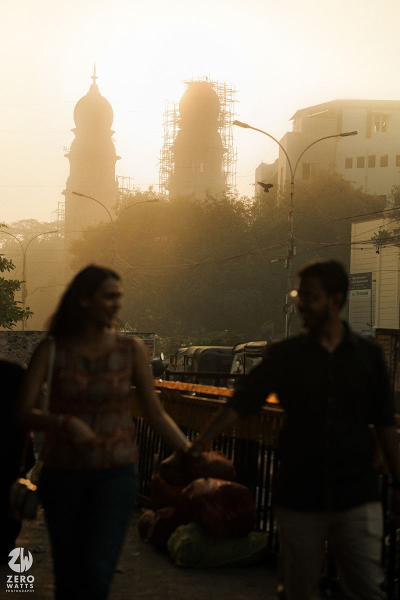Silhouettes of couple with mosque towers and scaffolding in misty sunset backdrop.