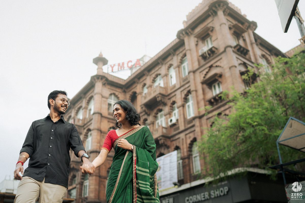 A couple in traditional and modern attire posing in front of a colonial-style building.