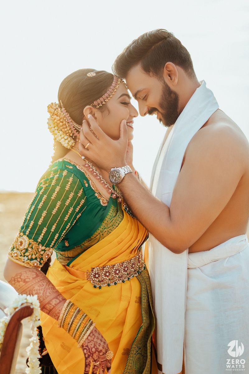 A couple in traditional Indian wedding attire share an intimate moment at sunset, with the bride wearing a yellow and green saree.