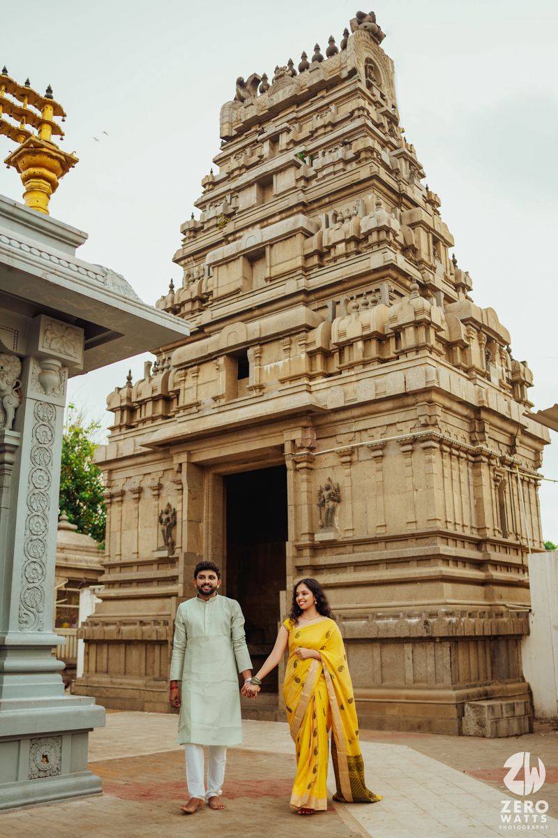 Couple in traditional Indian attire standing in front of ornate temple architecture.