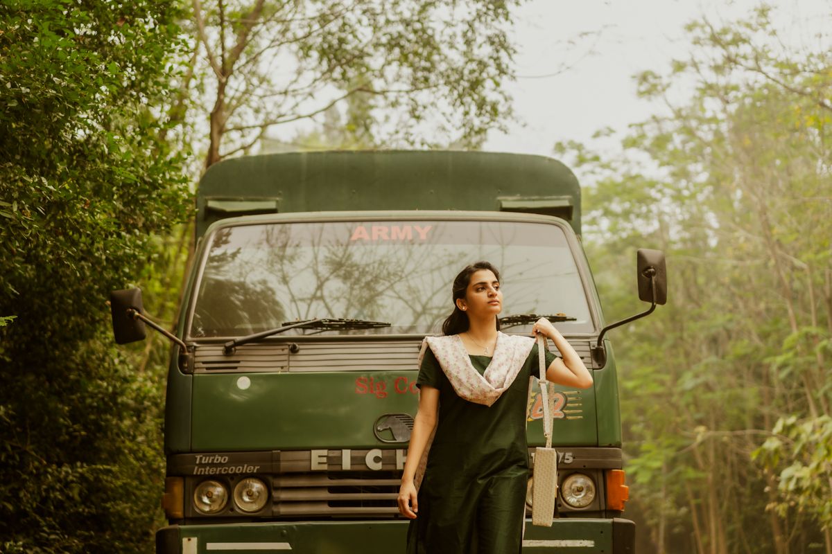 Person posing confidently in front of vintage green military truck in lush setting.