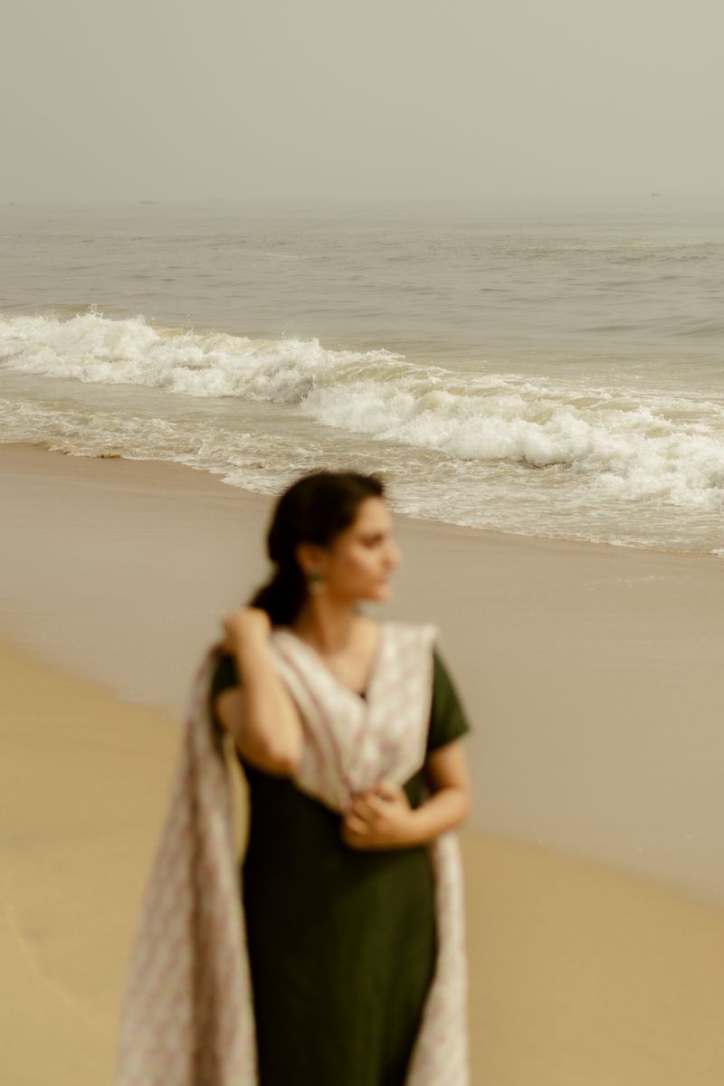 Person in traditional dress standing on beach with crashing waves in background.