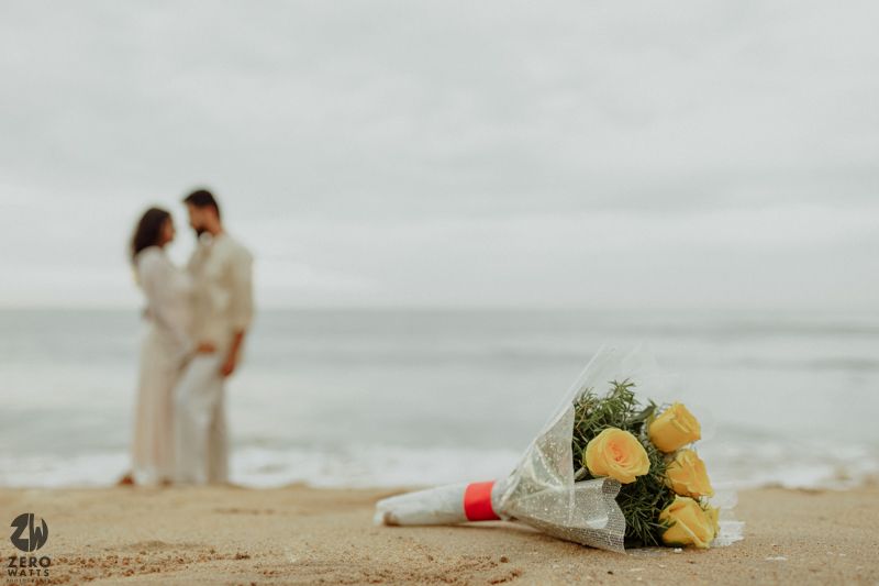 Yellow flowers lay on a misty beach with distant figures walking along the shoreline.