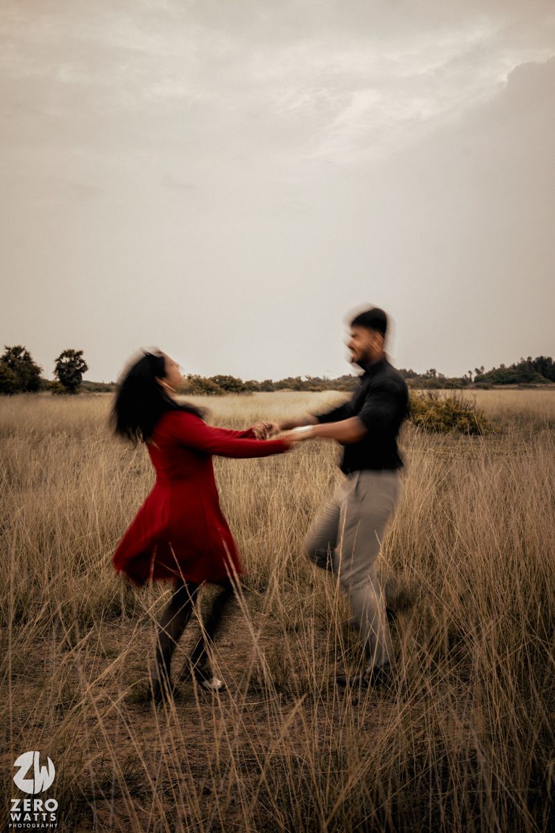 Two people dancing and spinning in a field of tall grass at dusk.