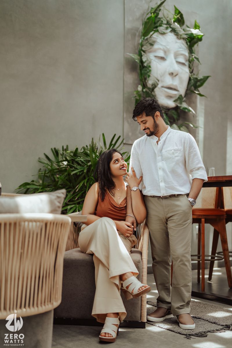Intimate indoor photoshoot scene with vintage furniture and tropical plants in the background.