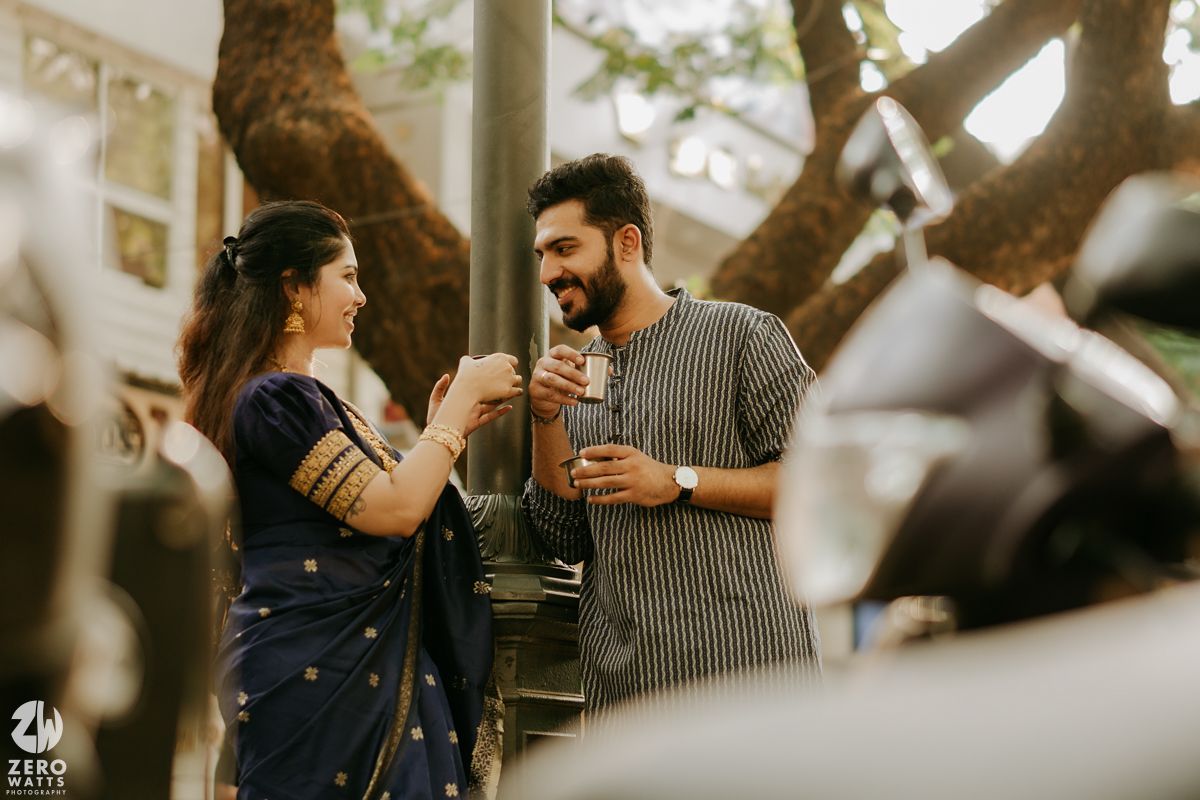 Two people sharing milkshakes and laughing together in front of a tree on a sunny afternoon.