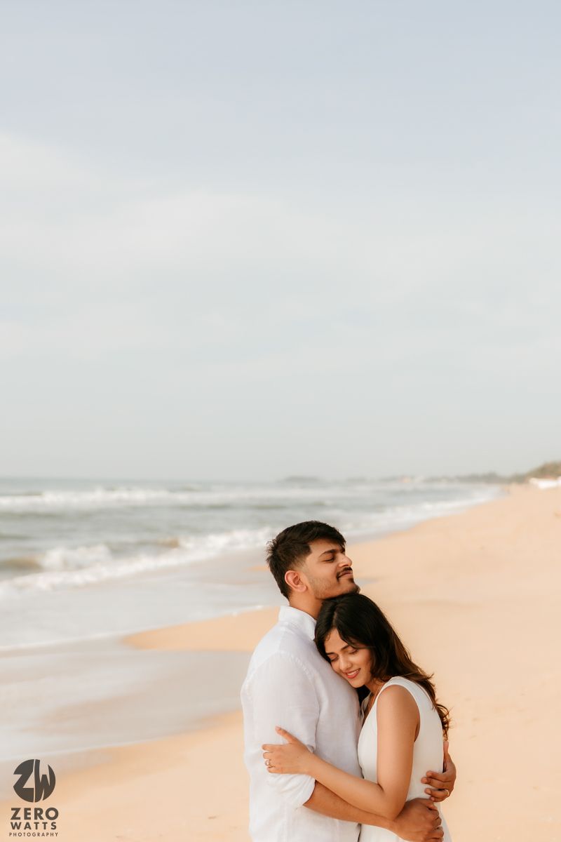 Intimate beach photo session with couple embracing against cloudy coastal backdrop.