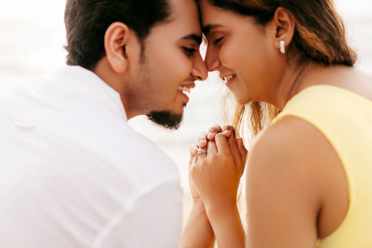 Close-up of couple sharing intimate moment on beach with foreheads touching.