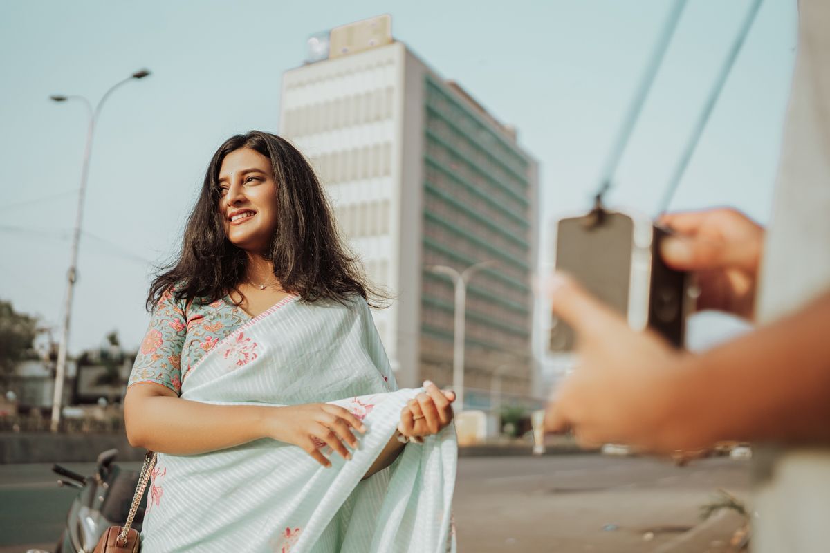 Woman in white dress smiles while standing on city street with urban buildings in background during golden hour.