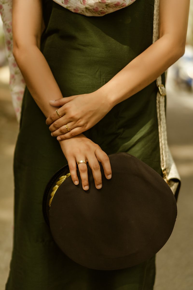 Close-up of hands holding a black hat while wearing an elegant green dress and floral dupatta.