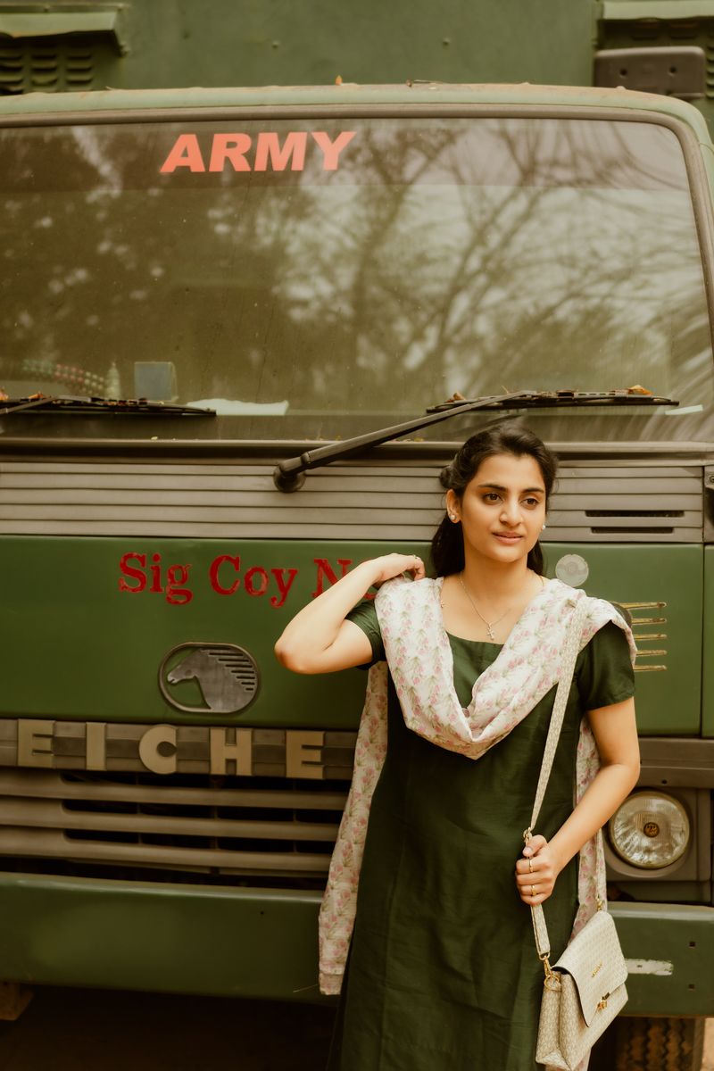 A woman poses in traditional dress next to an army vehicle, creating a striking contrast between military and civilian aesthetics.