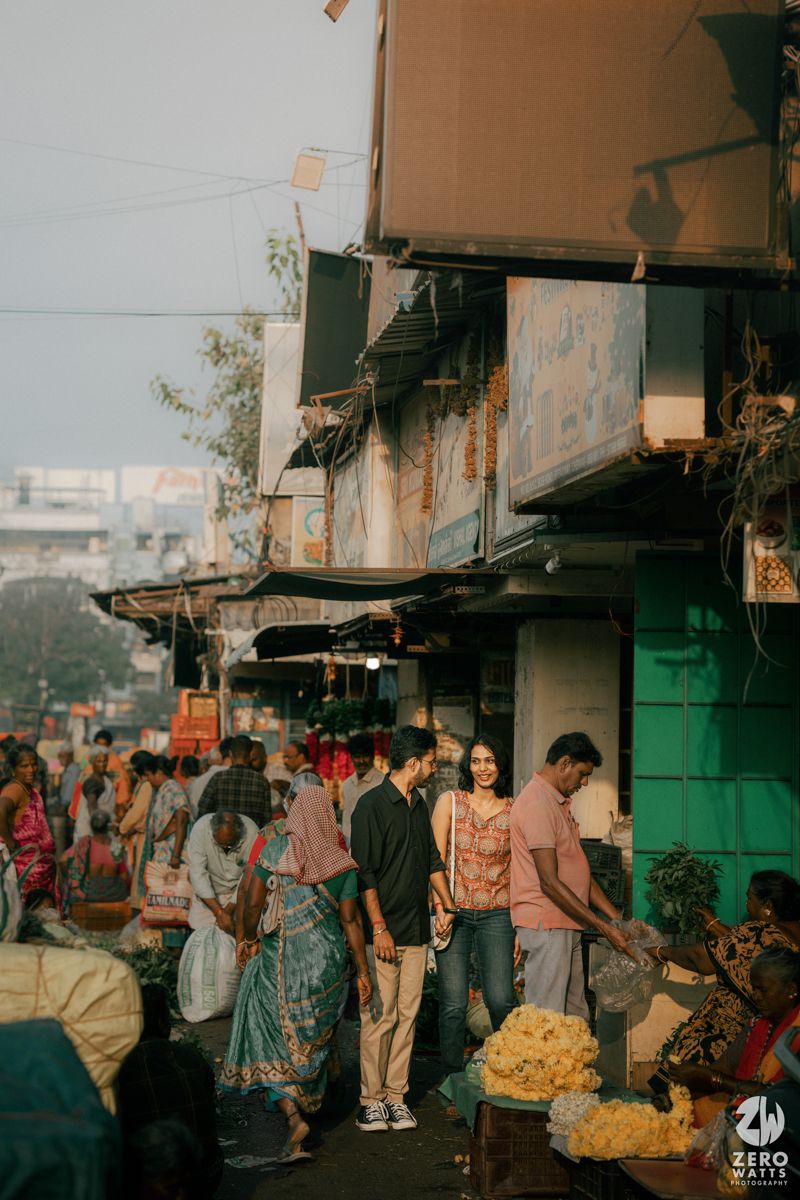 Bustling Indian street market scene with shoppers and vendors amid old buildings.
