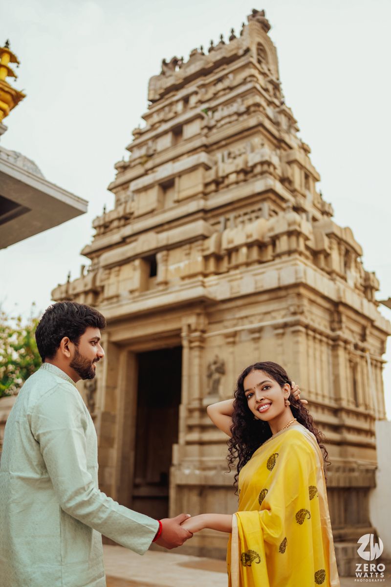 Two people in traditional attire share a romantic moment in front of an ornate temple gopuram in South India.